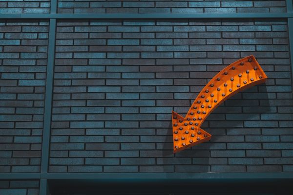 Orange arrow, on a brick wall, pointing down.